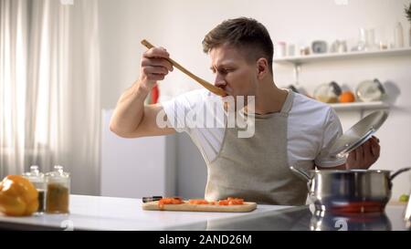 Uomo di degustazione zuppa cotta dalla padella, indossare un grembiule in cucina che prepara la cena Foto Stock