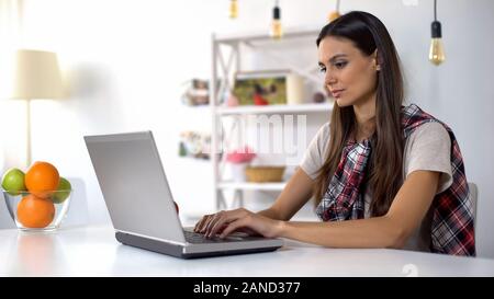 Giovani femmine freelancer lavorando sul computer portatile mentre è seduto sulla cucina, lavoro Foto Stock