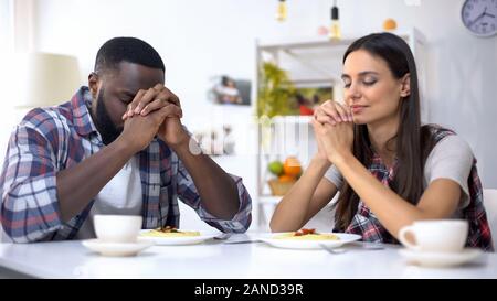 Giovane coppia multietnica pregare prima di pranzo, ringraziando Dio per pasto, religione Foto Stock