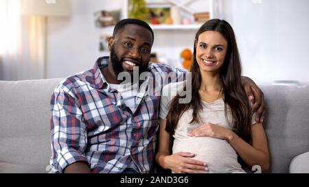 Multietnica giovane guardando la telecamera, donna incinta azienda ventre, ivf clinic Foto Stock