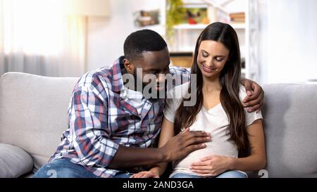 Sorridente uomo afro-americano di accarezzare la sua moglie incinta pancia, futuri genitori Foto Stock