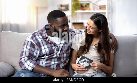 Gioiosa multirazziale giovane che guarda sul bambino x-ray, famiglia felice, aspettativa Foto Stock