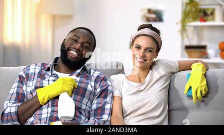 Sorridente mixed-gara giovane azienda detergente spray, felice circa il fatto lavori domestici Foto Stock