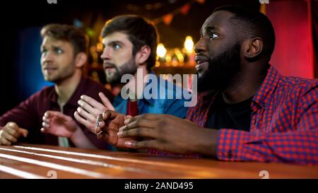 Tre amici multietnica guardando Song Contest sul tv in bar, pronto per applausi Foto Stock