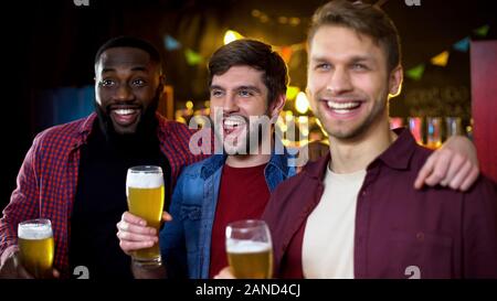 Sorridendo allegro amici maschi holding bicchieri da birra, team vittoria in campionato Foto Stock