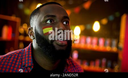 Sorpreso afro-americano con la bandiera spagnola sulla guancia guardando bed news Foto Stock