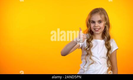 Funny schoolgirl mostrando pollice in alto isolato su sfondo arancione, modello Foto Stock