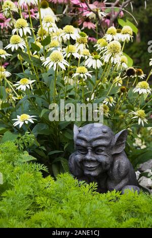 Close-up di grigio scuro gargoyle scultura e Echinacea 'Bianco' Lustre - Coneflowers nel confine del giardino nel cortile anteriore paese giardino d'estate. Foto Stock