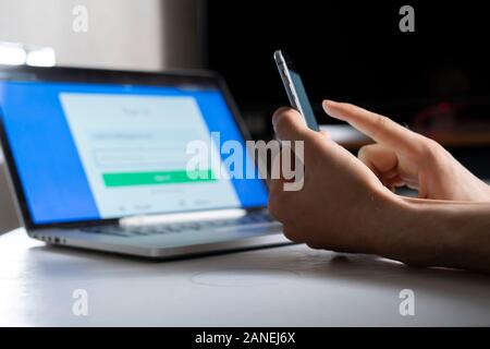 holding a phone and working using laptop, log in on website, double-factor authentication interface Foto Stock