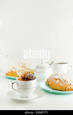 Spruzzi di tè in una tazza. Bianco tabe colazione con croissant freschi. Spazio di copia, verticale Foto Stock
