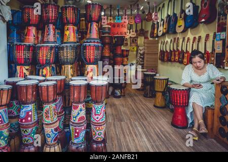 Feng Huang, Cina - Agosto 2019 : annoiato venditore femmina in attesa di clienti all'interno del suo strumento tradizionale e negozio musicale sulla strada in O Foto Stock