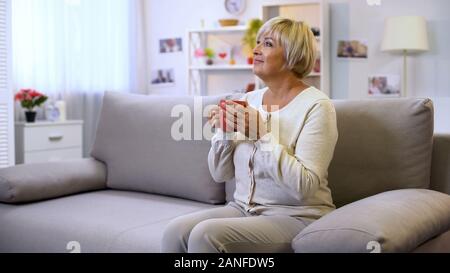 Bella Signora senior holding tazza da tè, seduto sul divano di casa, godendo di fine settimana Foto Stock