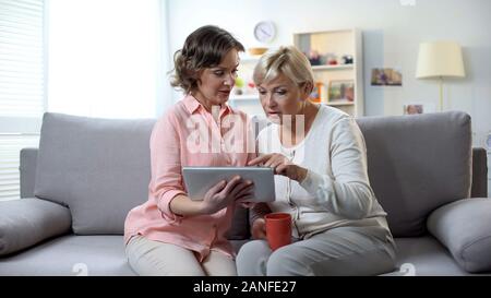Figlia di madre di insegnamento come utilizzare app bancario, seduto sul divano con tazza da tè Foto Stock