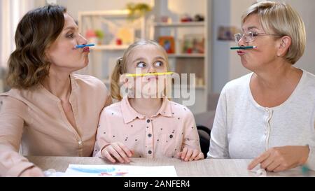 Funny multi-generazione femmine holding matite di colore tra il naso e le labbra, gioco Foto Stock