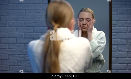 Giovane donna vestita in accappatoio di toccare la faccia nella disperazione, la sofferenza della depressione Foto Stock