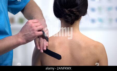 Fisioterapista applicando a forma di Y su nastri femmina spalla del paziente sollecitazione muscolare Foto Stock