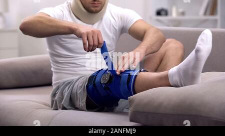 Uomo in schiuma collare cervicale in neoprene di fissaggio ortesi per ginocchio, seduto sul divano, rehab Foto Stock