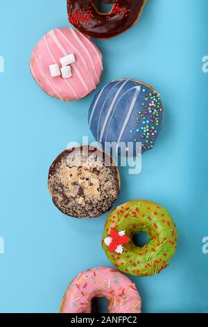 Dolce ciambelle colorate su sfondo blu, stabiliti nella forma di varie geomitric figura, la freccia, quadrato, linea, triangolo, vista dall'alto. I dessert, gioco o Foto Stock