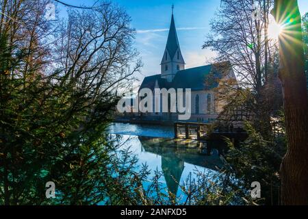 Germania, nebbia mattutina si spostano su acqua blu superficie della pentola blu o tedesco blautopf a Blaubeuren forest riflettendo bella chiesa edificio in Foto Stock