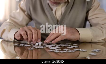 Senior uomo raccolta di puzzle, la malattia di Alzheimer consapevolezza esercizio di concentrazione Foto Stock