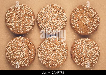 Farina di avena cookie sulla carta da forno. Pasticceria artigianale con semi di sesamo. Sfondo marrone. Un gruppo di biscotti Foto Stock