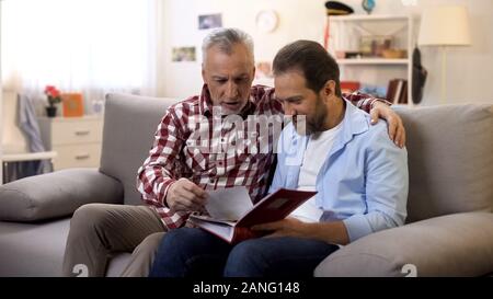 Adulto padre e figlio la visualizzazione di vecchie foto di condivisione di buone memorie tradizioni di famiglia Foto Stock