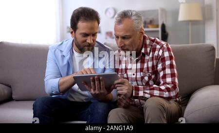 Pensionato padre e persone di mezza età figlio scheda scrolling, guardando le foto dalle vacanze Foto Stock