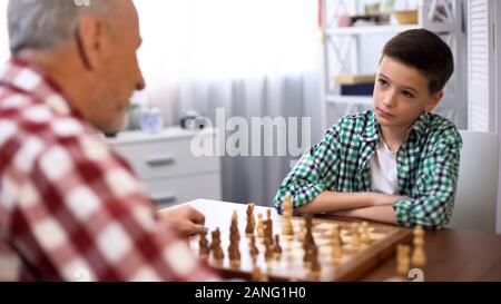 Giovane ragazzo giocando a scacchi con il nonno, tradizioni familiari, lo sviluppo della mente Foto Stock