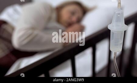 Dropper close-up, malati donna che dorme nel letto di ospedale sullo sfondo, la terapia Foto Stock