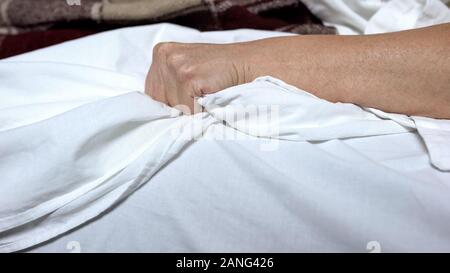 Terminalmente-ill donna clenching bedsheets sensazione terribile dolore e morte convulsioni Foto Stock