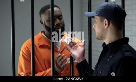 Jail guard dando afro-americano pacchetto prigioniero con le pillole, attività illegali Foto Stock