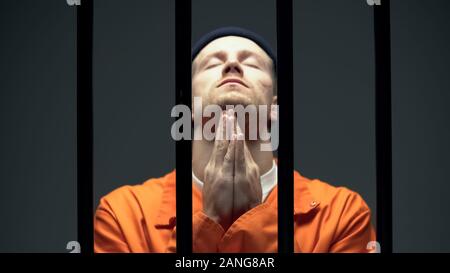 Uomo imprigionato nella disperazione pregando dietro le barre di cella, si senta in colpa riguardo al fatto di reato Foto Stock