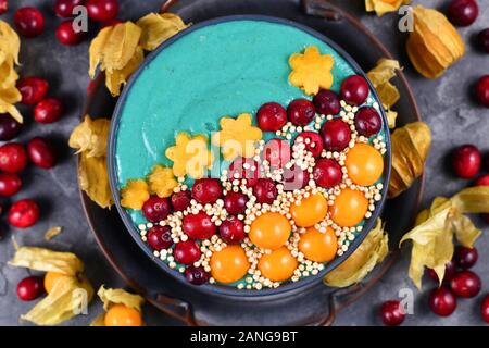 Vista superiore del sano yogurt e frutta smoothie ciotola con verde naturale spirulina in polvere e decorate con mirtilli rossi, physalis e kaki Foto Stock