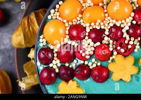 Dettaglio di un sano yogurt e frutta smoothie ciotola con verde naturale spirulina in polvere e decorate con mirtilli rossi, physalis e kaki Foto Stock