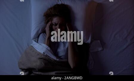 La donna che soffre di terribili mal di testa che giace nel letto di notte, vita nelle grandi città Foto Stock