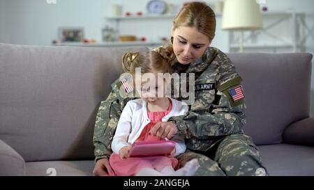 Militare insegnamento madre bambina gioca sul giocattolo tablet, educativo gadget Foto Stock