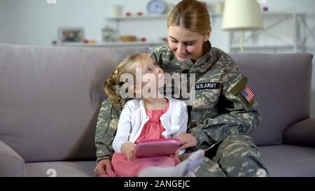 Madre in US Army uniforme e piccola figlia giocando su tablet insieme Foto Stock