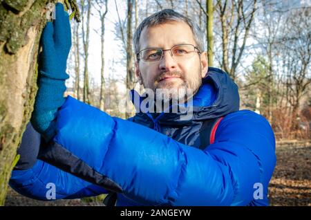 Uomo di mezza età in blue Down Jacket rilassante nella foresta Foto Stock