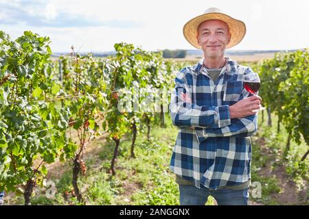 L'uomo come un viticoltore soddisfatto con un bicchiere di vino rosso nella sua cantina Foto Stock
