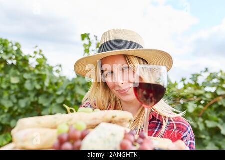 La donna come un raccolto di lavoratori con un bicchiere di vino rosso e uva per un picnic Foto Stock
