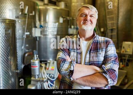 L'uomo come un produttore o enologo in una birreria o cantina nella parte anteriore di un serbatoio di fermentazione Foto Stock