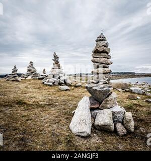 Diversi artificiali in pietra in granito di pile (chiamato cairns) sul sentiero costiero in Bretagna, Francia, in un giorno nuvoloso. Foto Stock