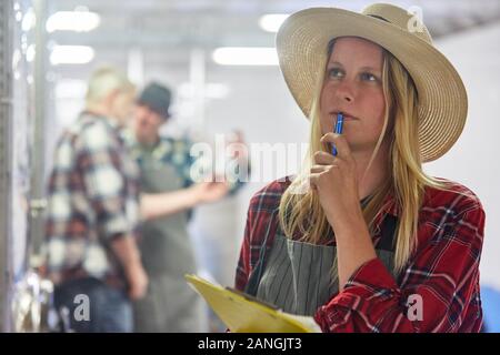 Giovane donna come un enologo partecipante con la lista di controllo nella cantina di serbatoio di fermentazione Foto Stock