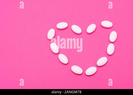 Bianco pillole ovale giacciono su sfondo rosa. Spazio di copia, macro Foto Stock
