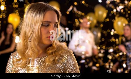 Sconvolto woman standing a parte sola, tenendo champagne vetro, problema di relazioni Foto Stock