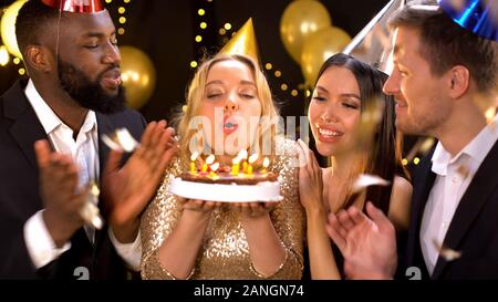 Femmina allegro godendo il compleanno con gli amici vicini soffiando fuori le candele per torta Foto Stock