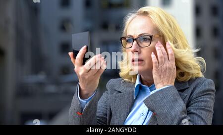 Preoccupato per il business donna guardando le rughe degli occhi mano, specchio anti-invecchiamento cosmetici Foto Stock