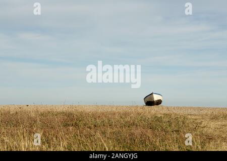 Una barca a sinistra sulla spiaggia di ghiaia a Suffolk, East Anglia, Inghilterra Foto Stock