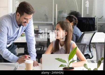 Diversi colleghi ridere discutere di affari progetto al computer portatile in ufficio condiviso insieme, millenaria uomo e donna sorriso di parlare mentre si considera ide Foto Stock