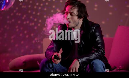 Idle giovane vaping e-sigaretta ad alleviare lo stress, rilassante presso la discoteca party Foto Stock